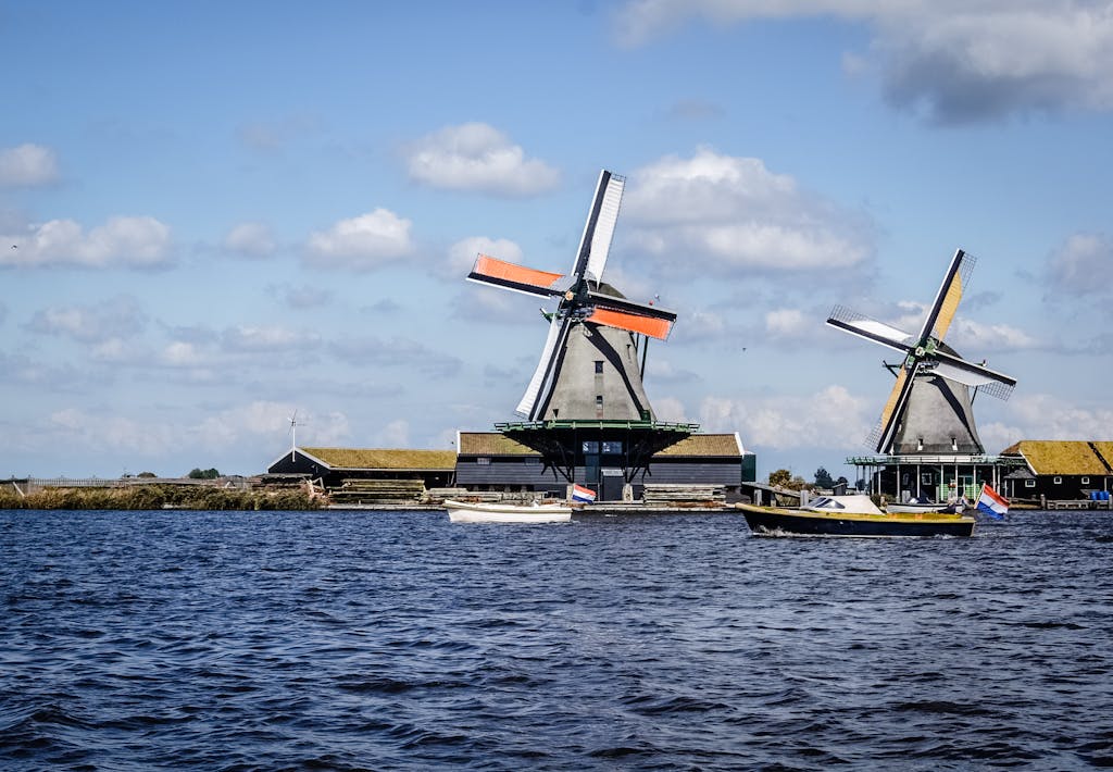 Scenic view of traditional Dutch windmills near water under a blue sky with clouds.